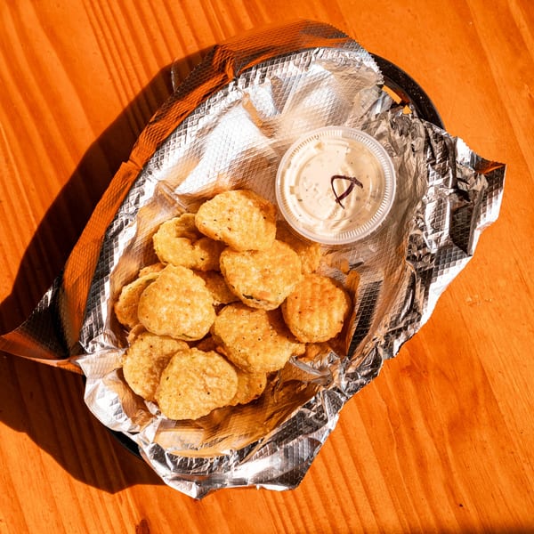 A basket of Fässer's fried pickles with a side of ranch dressing on a wooden table.