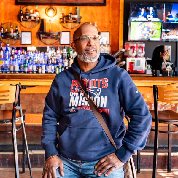 Man in a Patriots hoodie sitting at the Fässer bar, with bottles and TVs in the background.