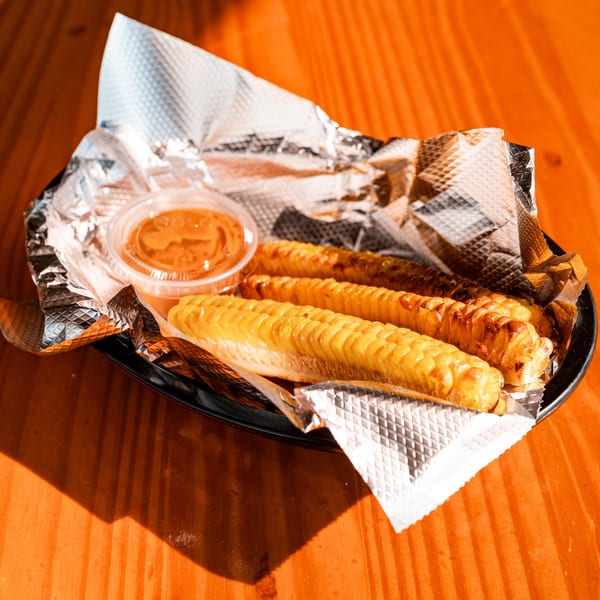 Three grilled corn on the cob with a side of sauce in a foil-lined basket.