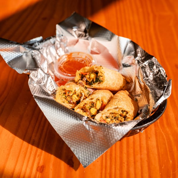 Fässer's crispy egg rolls filled with corn and vegetables, served with dipping sauce in a foil-lined basket.
