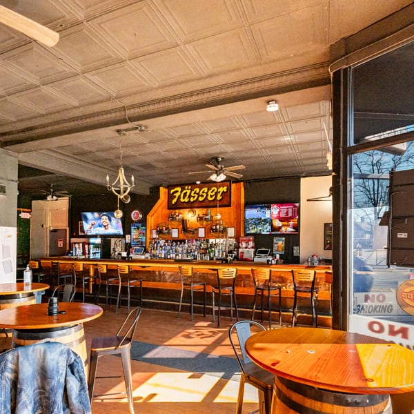 Interior of Fässer bar-&-grill with a long wooden bar, stools, and barrel tables.